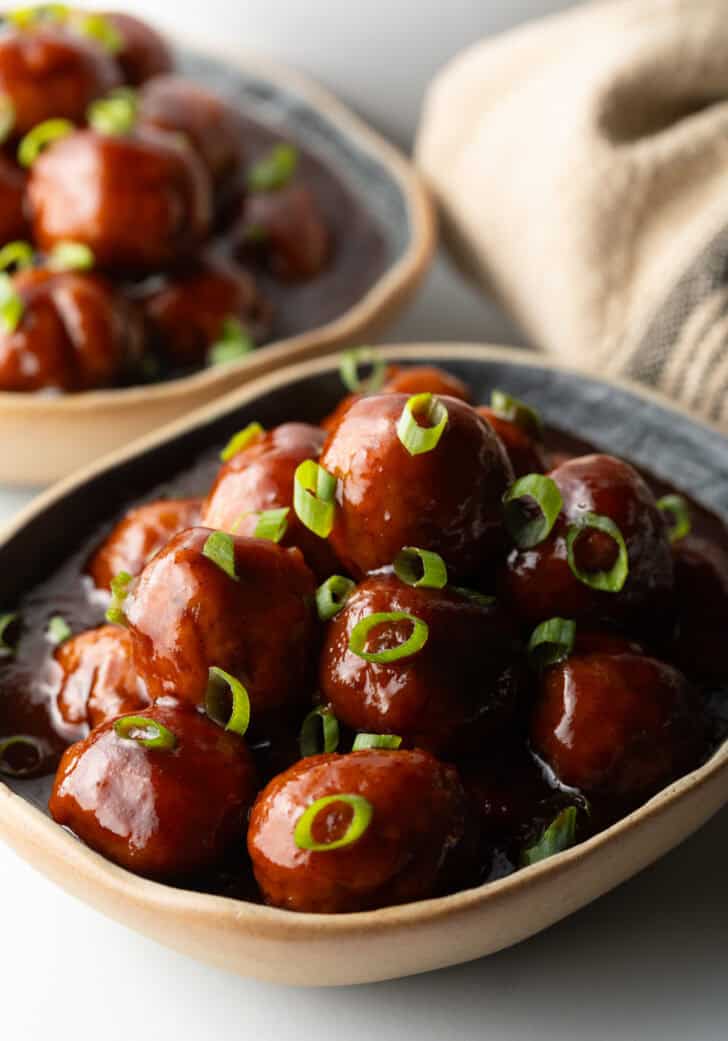 Bowl full of meatballs covered in barbecue sauce, topped with fresh chopped scallions.