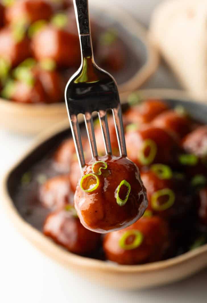 A fork is holding a bbq sauce-coated meatball to camera.