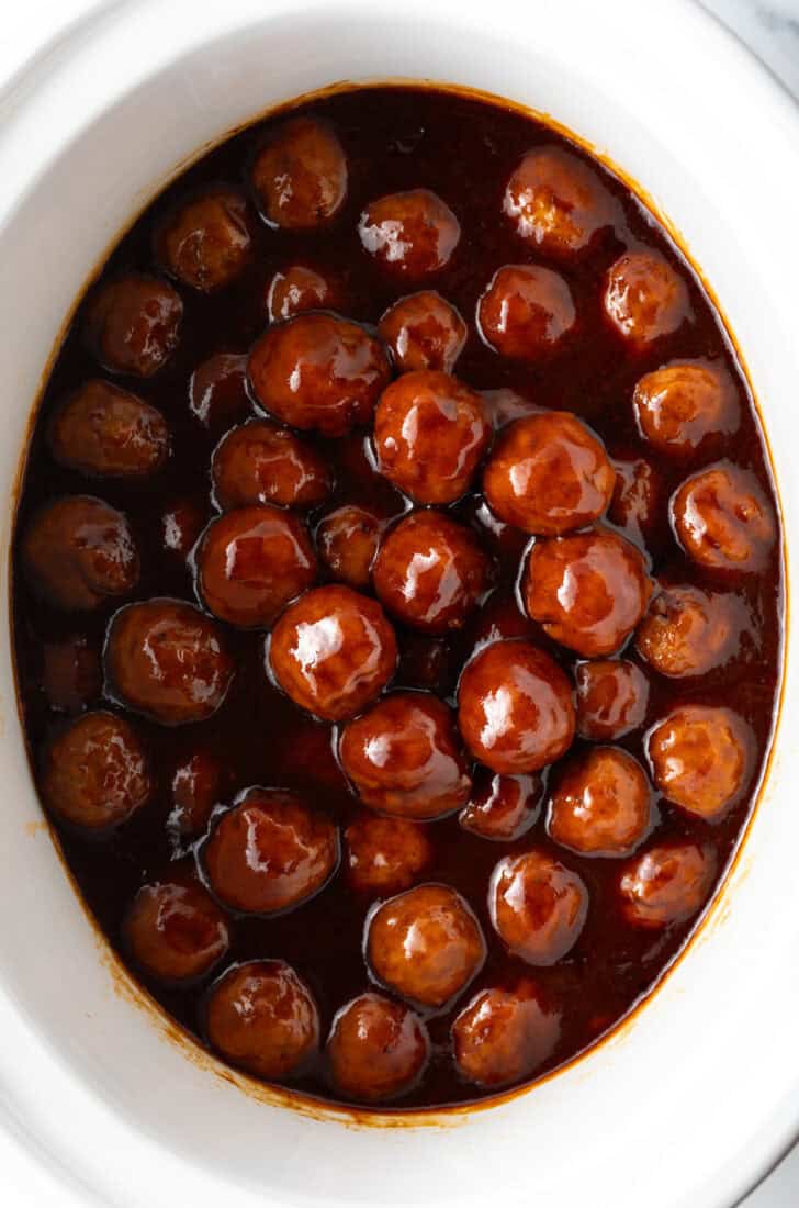 White slow cooker filled with meatballs in bbq sauce.