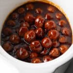 White slow cooker filled with meatballs in bbq sauce.