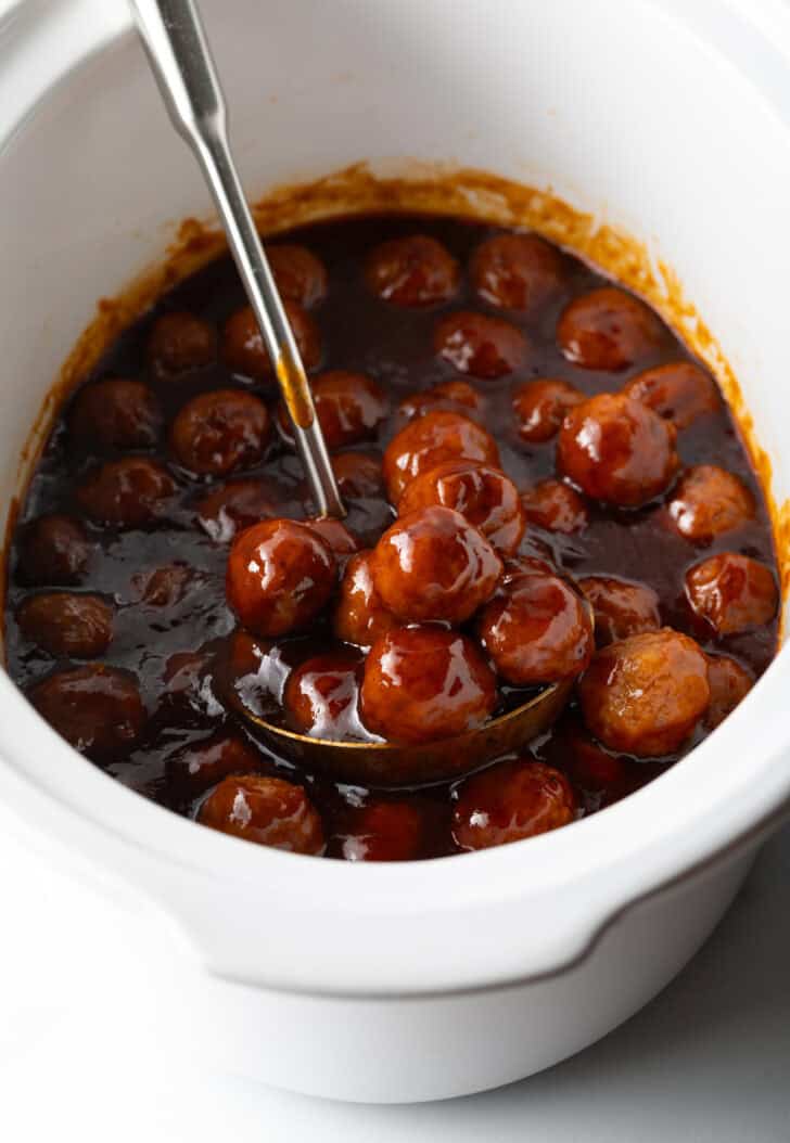 White slow cooker filled with meatballs in bbq sauce.