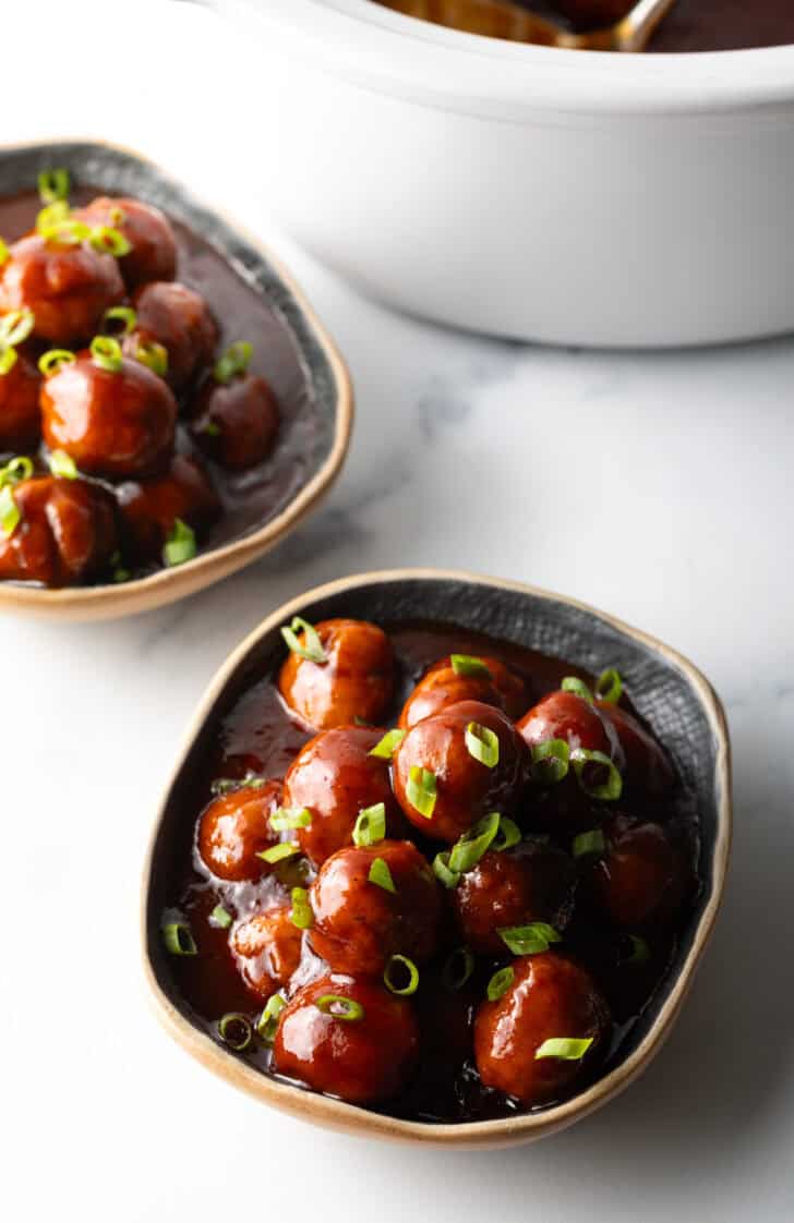 Bowl full of meatballs covered in barbecue sauce, topped with fresh chopped scallions.