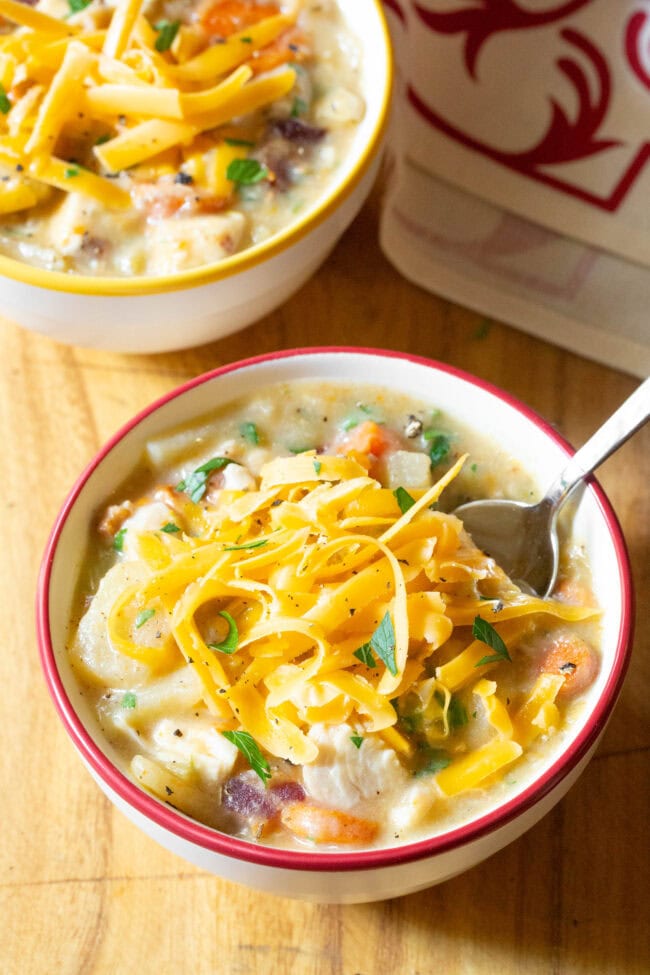 Two bowls of chicken potato soup topped with shredded cheese.