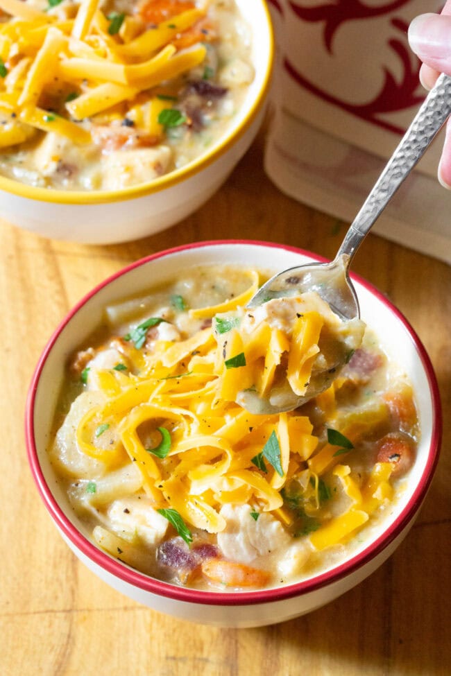 Crockpot Potato soup in a bowl with a hand holding a spoon scooping up a bite.