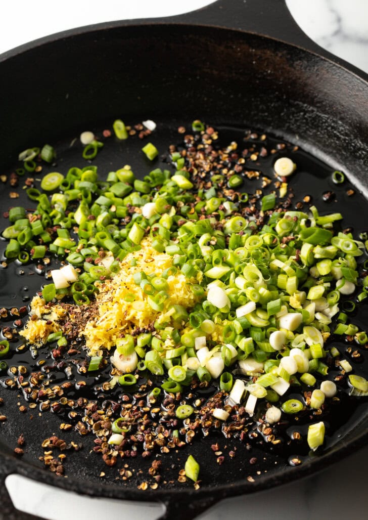 Spicy Szechuan peppercorns, ginger, and green sliced onions in a cast iron skillet.