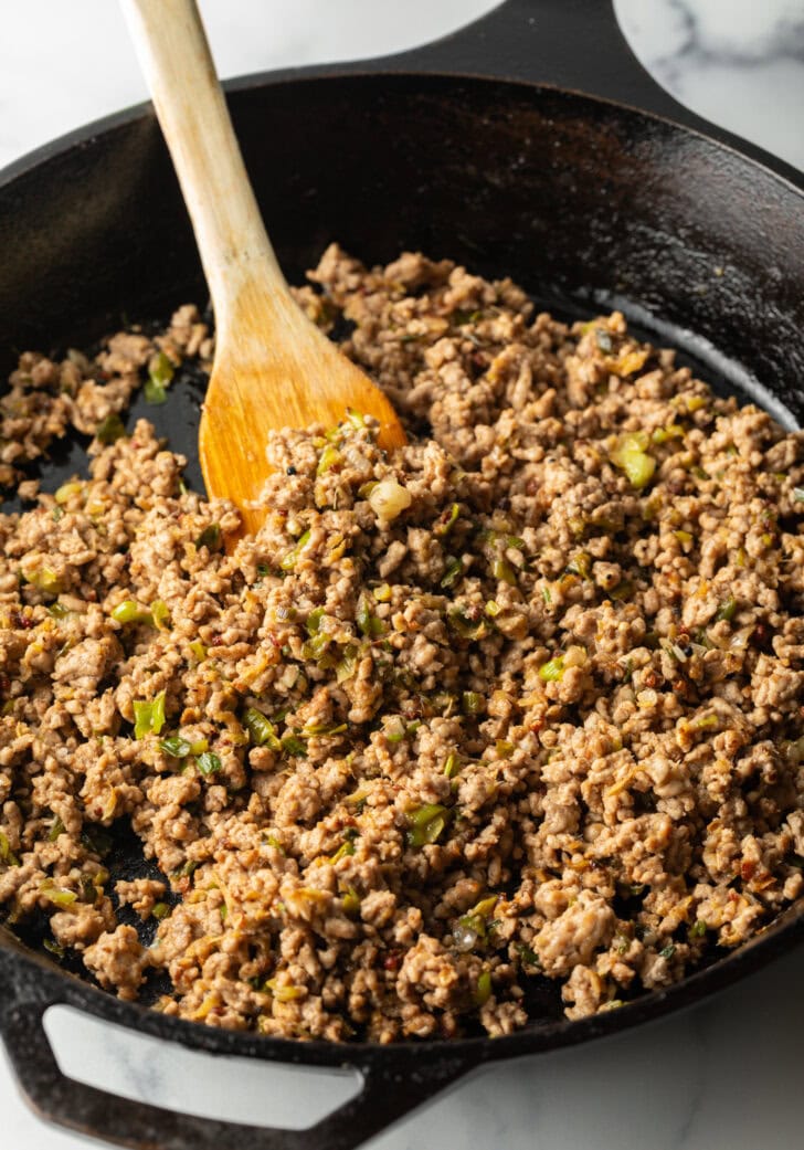 Cooking ground pork in a cast iron skillet with wooden spoon.