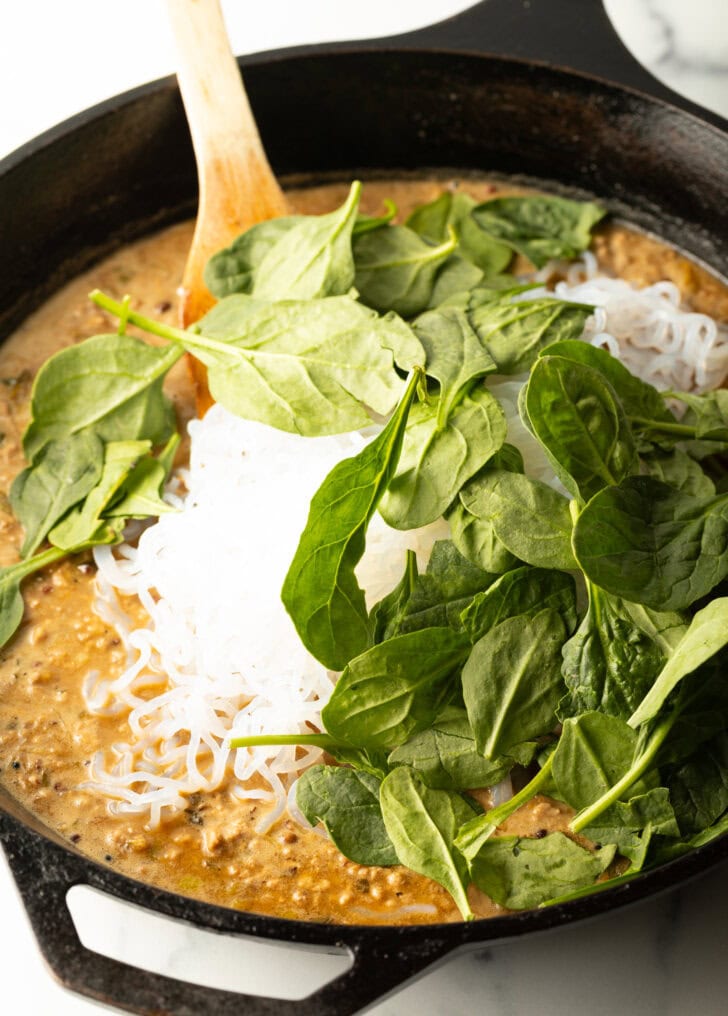 Adding low carb noodles and fresh spinach to the skillet.