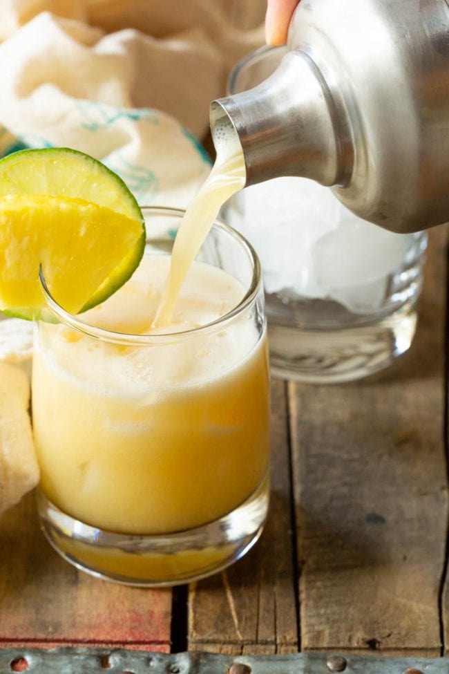 Pouring out this shaken rum cocktail into a juice glass 
