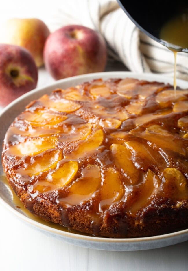 Upside down apple cake on a serving plate with whiskey sauce being poured on top. 