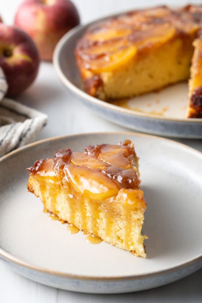 Slice of apple upside down cake on a white plate with whiskey sauce on top.