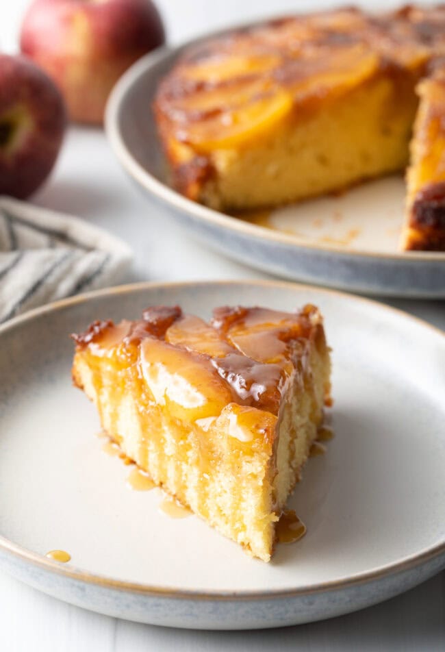 Slice of apple upside down cake on a white plate.