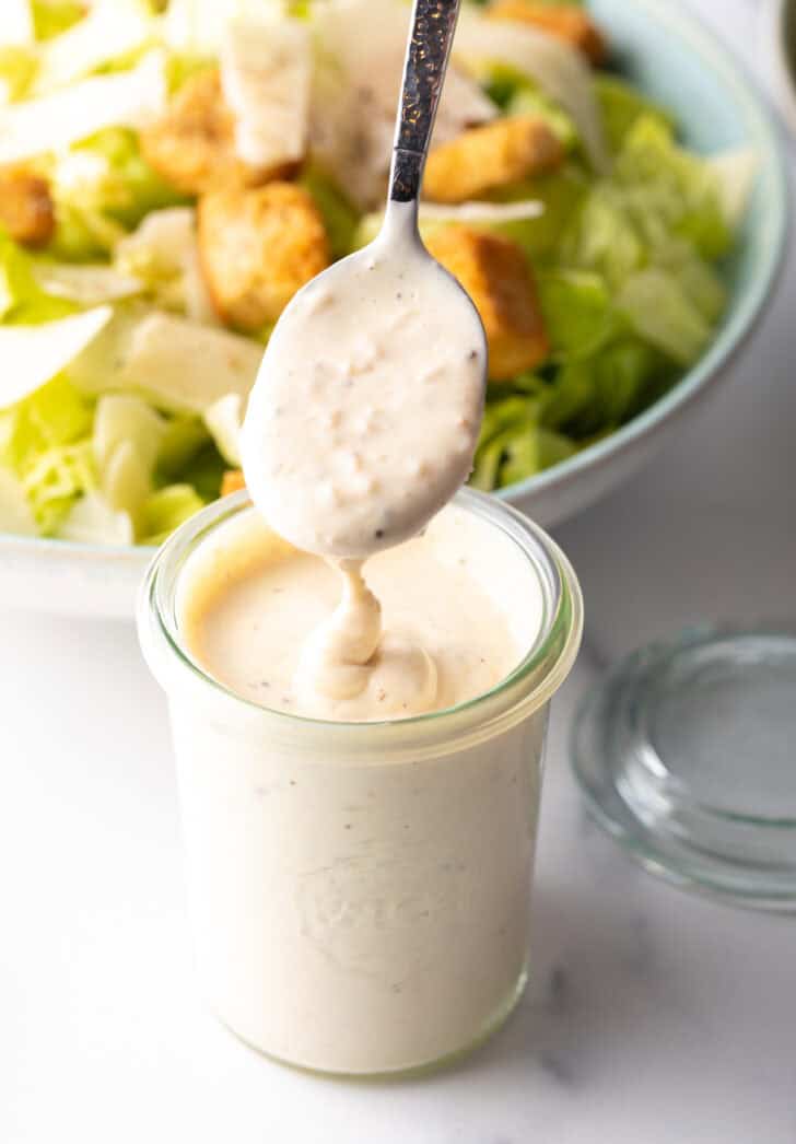 Showing a spoonful of dressing from a glass jar of Caesar.