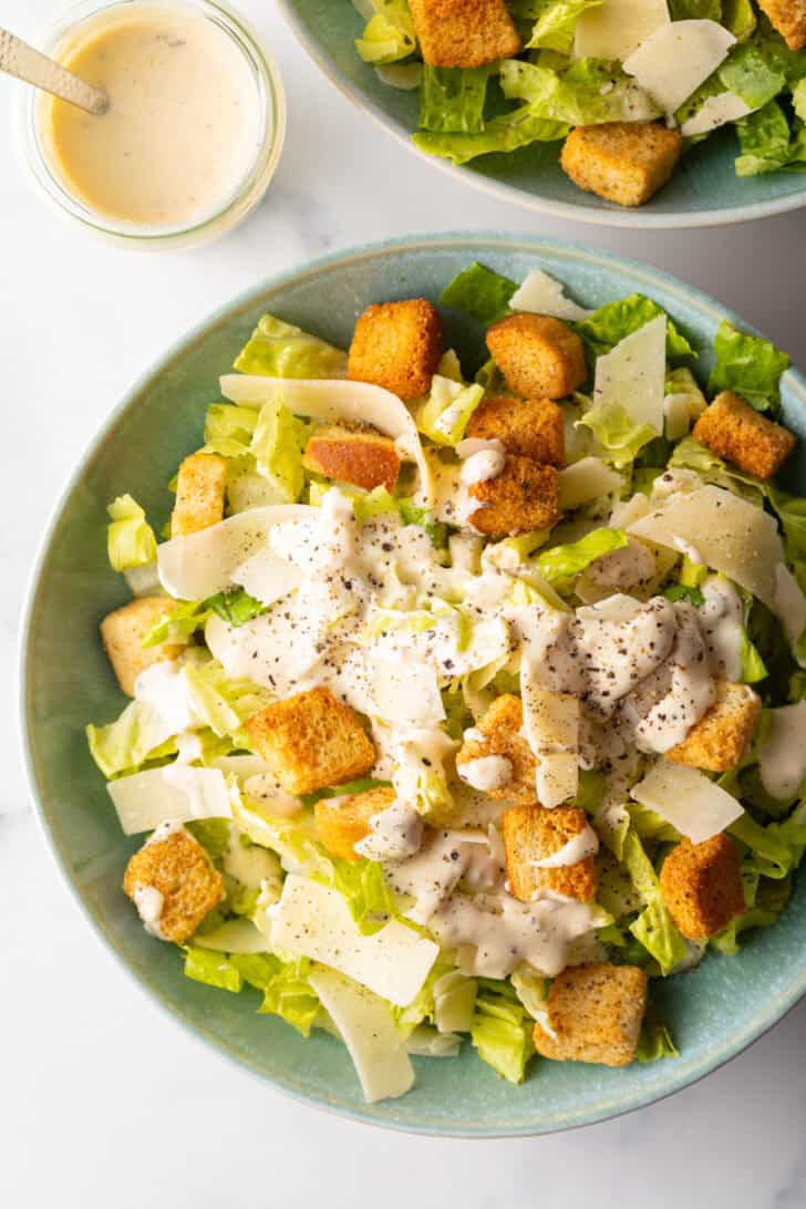 Top down view of a salad made with chopped romaine, croutons, and parmesan cheese. The salad is topped with a drizzle of homemade Caesar dressing.