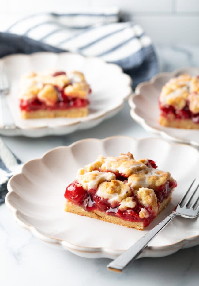 Three pieces of cherry pie bars on individual white scalloped plates.