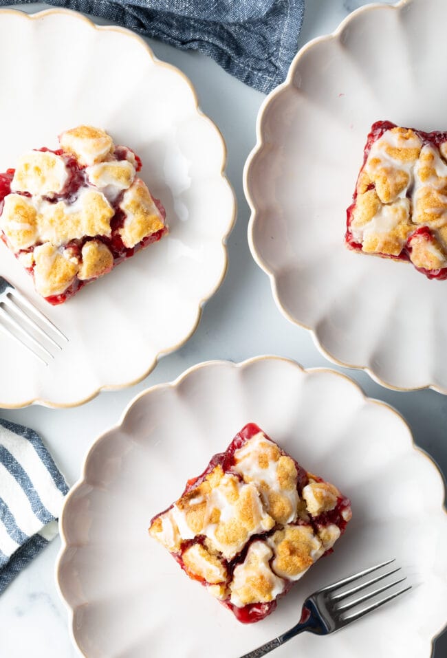 Top down three pieces of cherry pie bars on individual white scalloped plates.