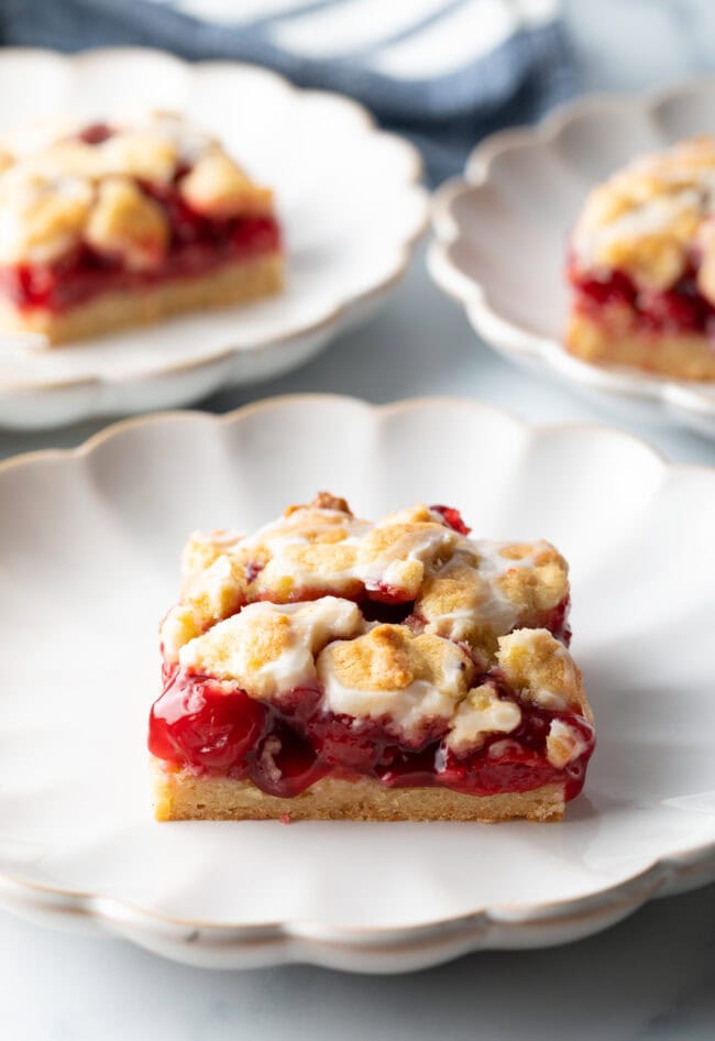 Square piece of cherry pie bar on a white scalloped plate.