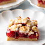 Square piece of cherry pie bar on a white scalloped plate.