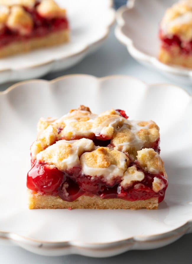 Square piece of cherry pie bar on a white scalloped plate.