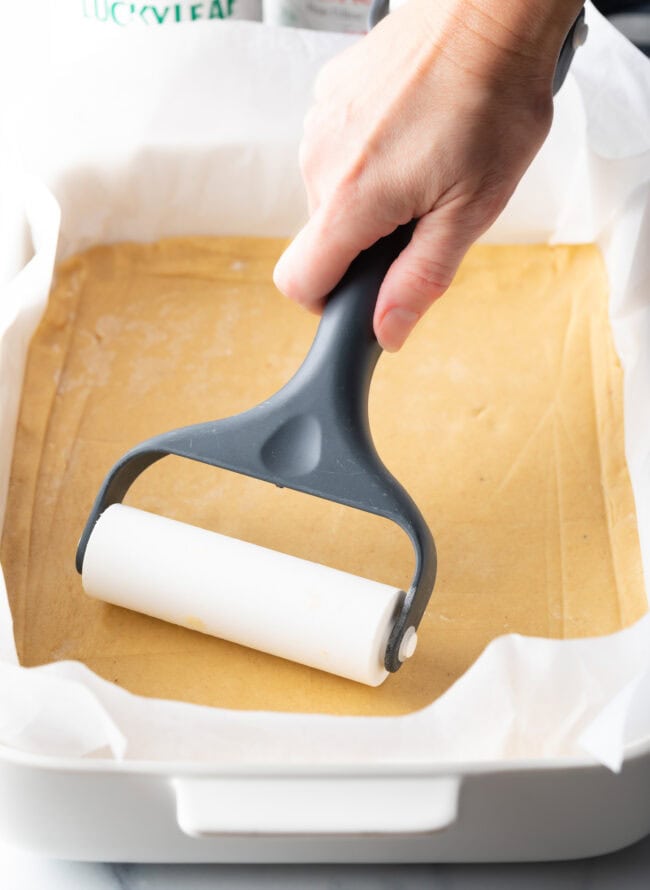 Hand with pastry roller, smoothing out a rectangle of dough into a baking pan.