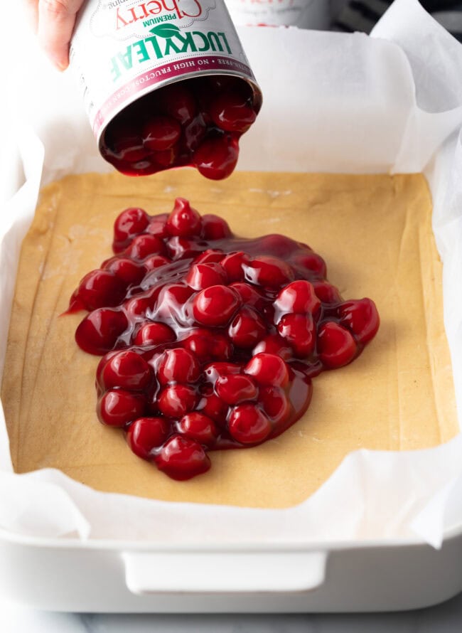 Can of cherry pie filling for desserts being added to rectangle baking dish with dough.