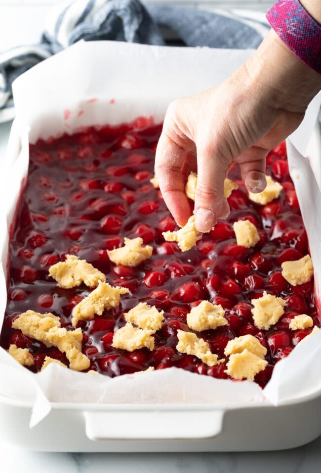 Hand adding raw dough pieces to the top of the pie filling.