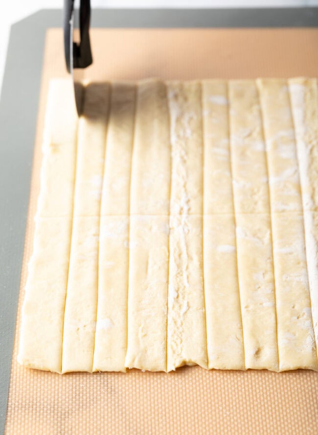 Pie cutter slicing puff pastry dough into thin even strips.