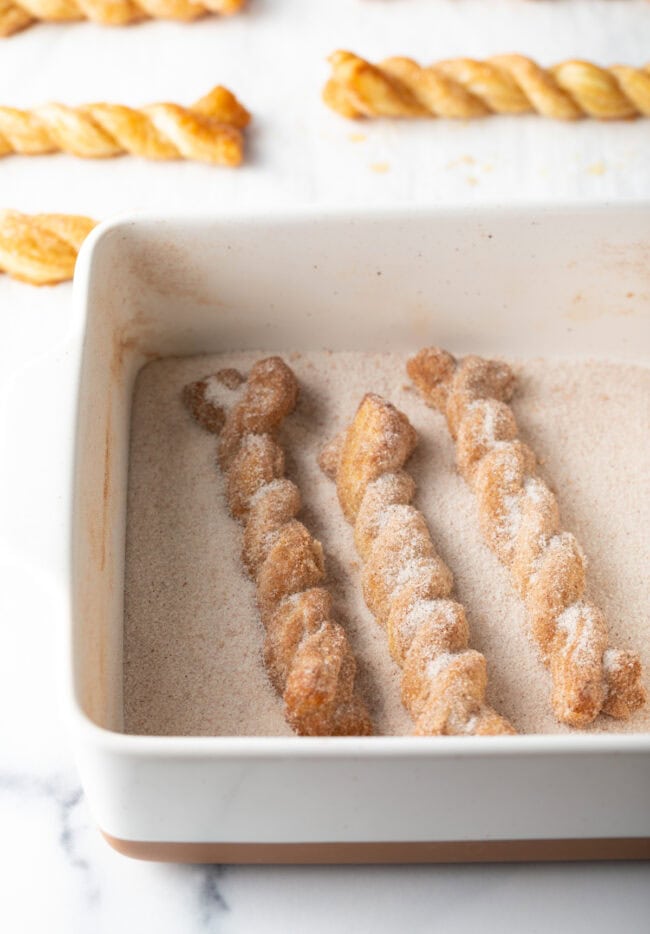 Baked cinnamon twists going into the cinnamon sugar mixture for second coating.