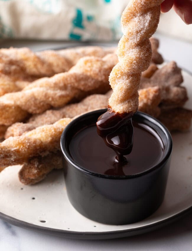 Dunking crispy cinnamon twist recipe into a ramekin of dark chocolate sauce.