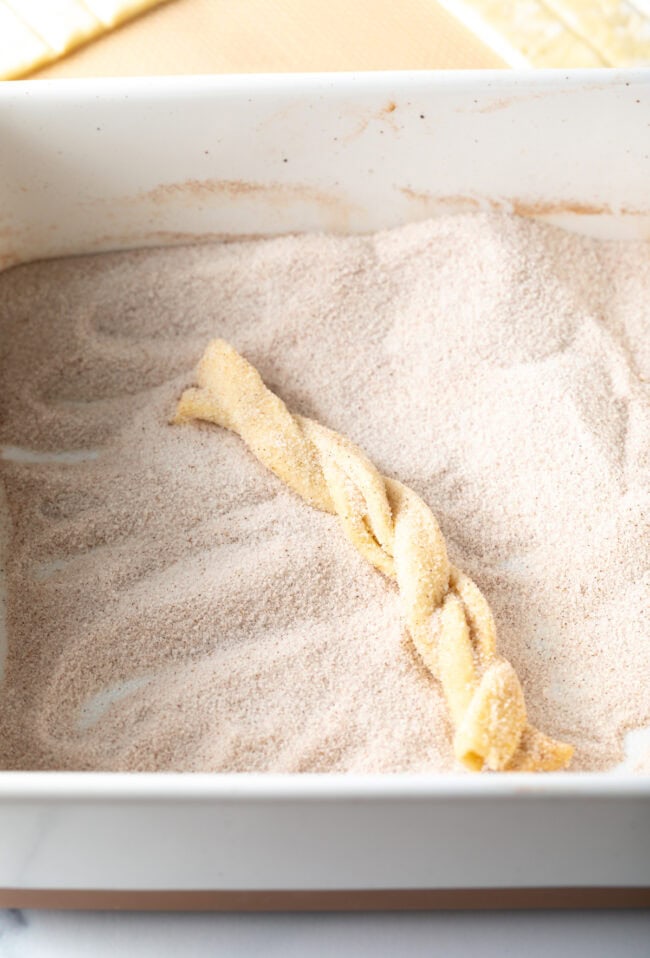 Tossing the unbaked pastry twist in cinnamon and sugar.