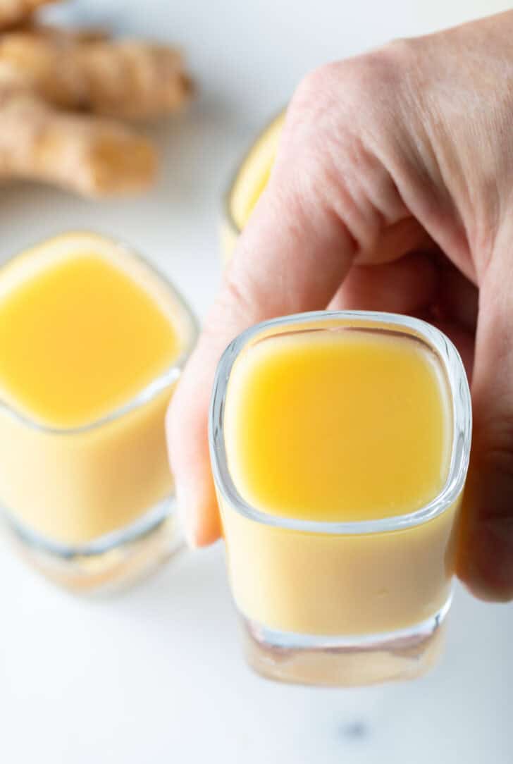 Hand holding a shotglass with yellow liquid to camera.