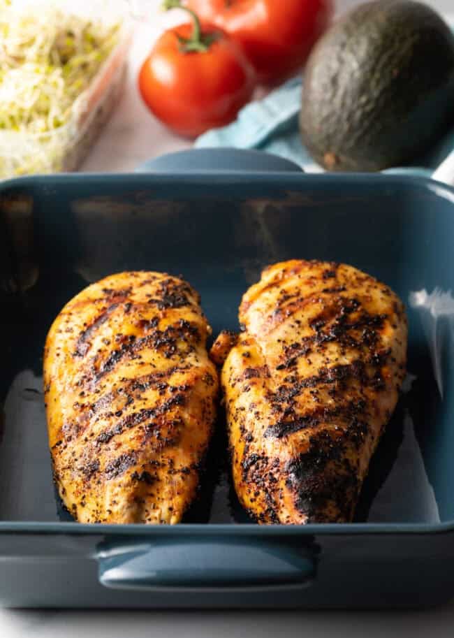 Two large grilled chicken breasts in a blue square baking dish.