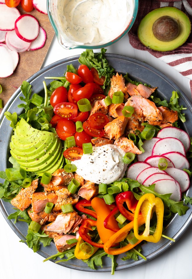Top down view grilled salmon salad recipe completed with veggies and dressing.