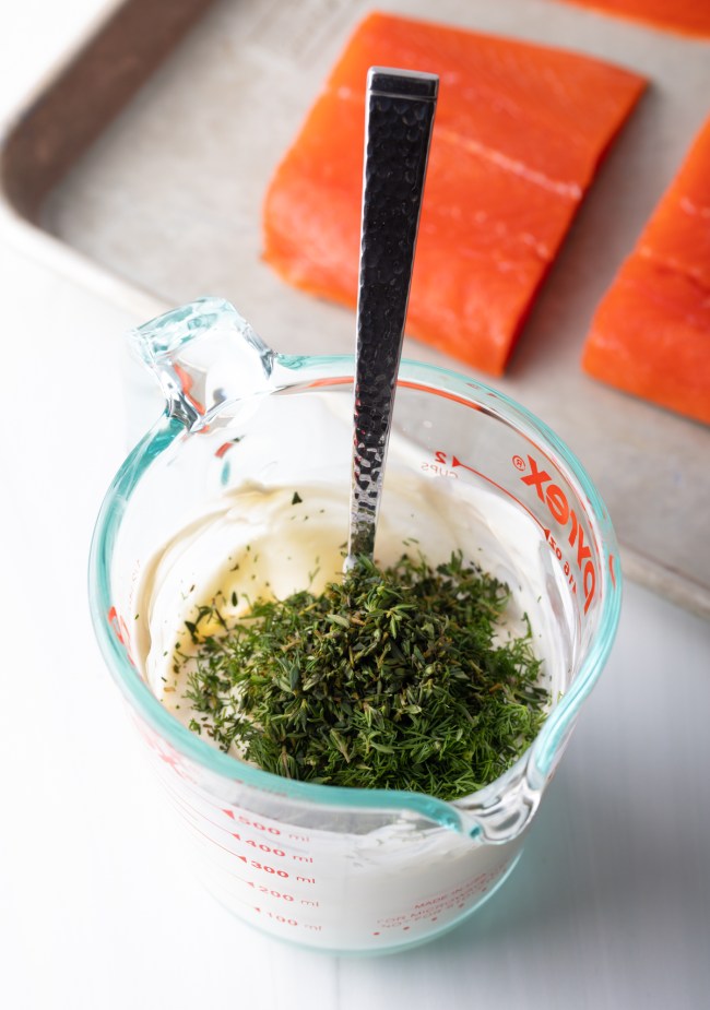 Glass measuring cup with mayo and fresh herbs.