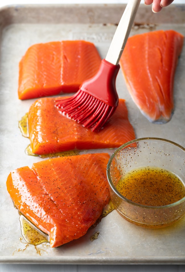 Basting raw salmon fillets with marinade of honey, vinegar, and spices.