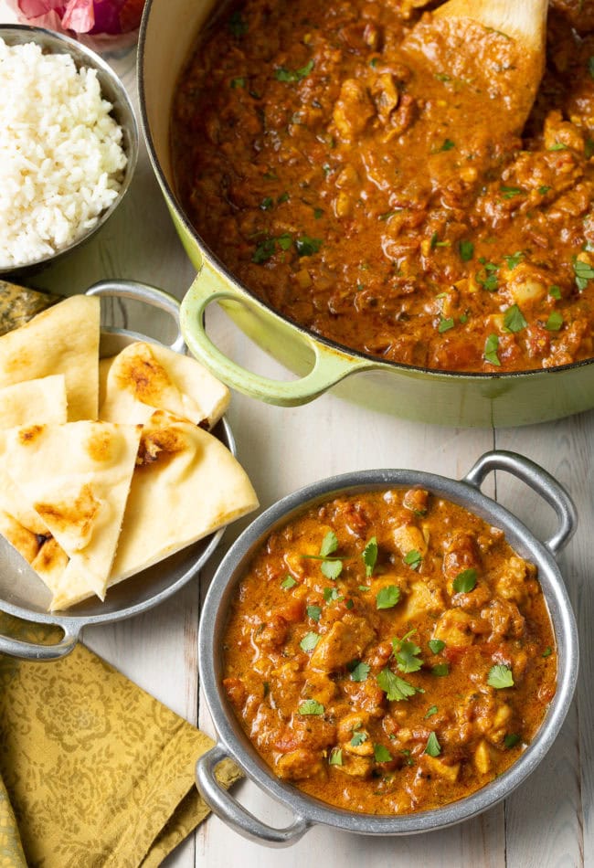 Madras-style chicken curry in a bowl next to naan bread. 