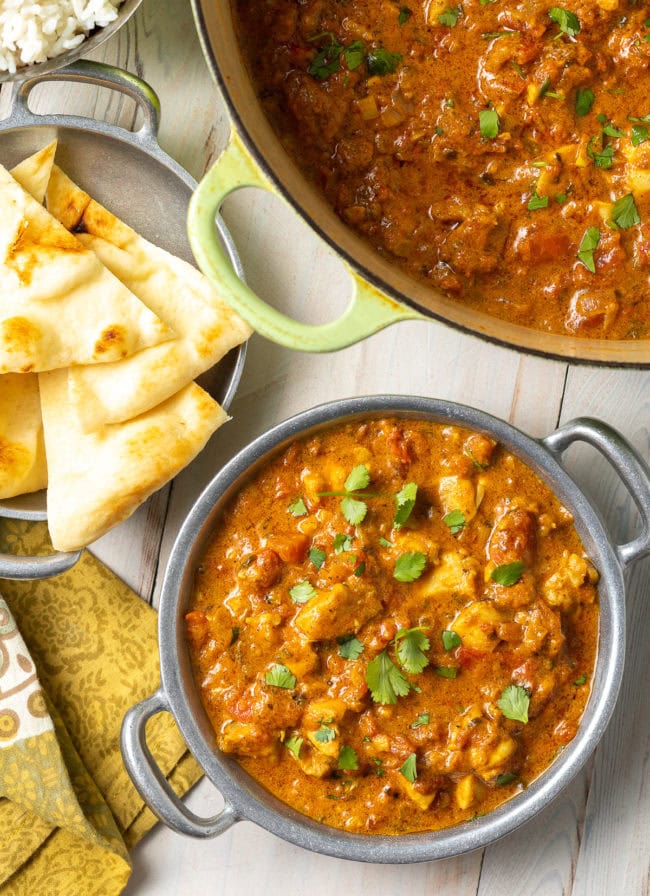 Easy Chicken Curry Recipe - Madras curry in a Dutch oven with more in a bowl next to some naan bread. 