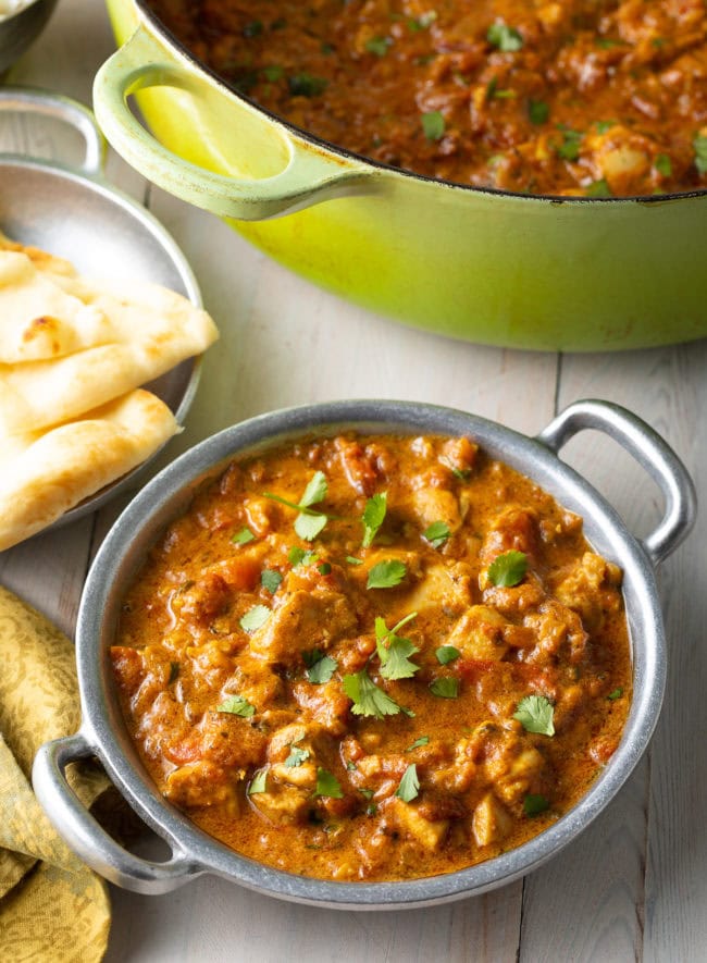 Easy Chicken Madras Curry in a silver bowl next to naan bread and a dutch oven. 