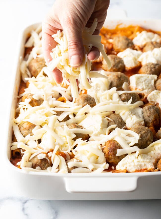 Hand adding shredded mozzarella to the casserole.