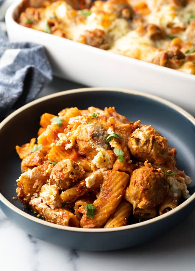 Dark gray plate with a generous portion of baked meatball casserole with pasta and cheese.