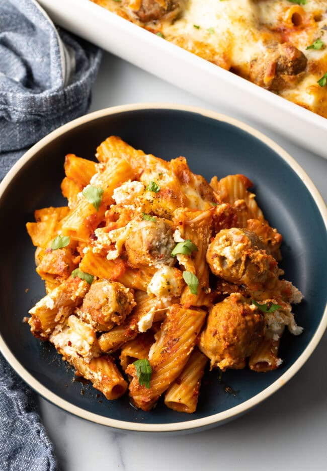 Dark gray plate with a generous portion of baked meatball casserole with pasta and cheese.