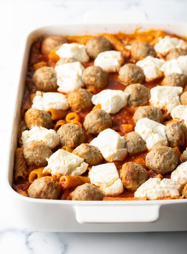 Layers of meatballs and chunks of cream cheese in marinara sauce, in white baking dish.