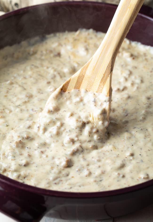 Stirring Easy Sausage Gravy Recipe in a skillet with a wooden spoon.