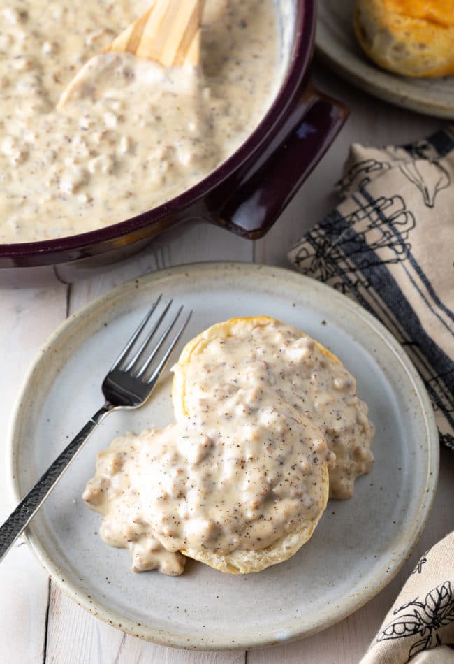 Biscuit on a plate smothered in spicy sausage gravy with a fork. 