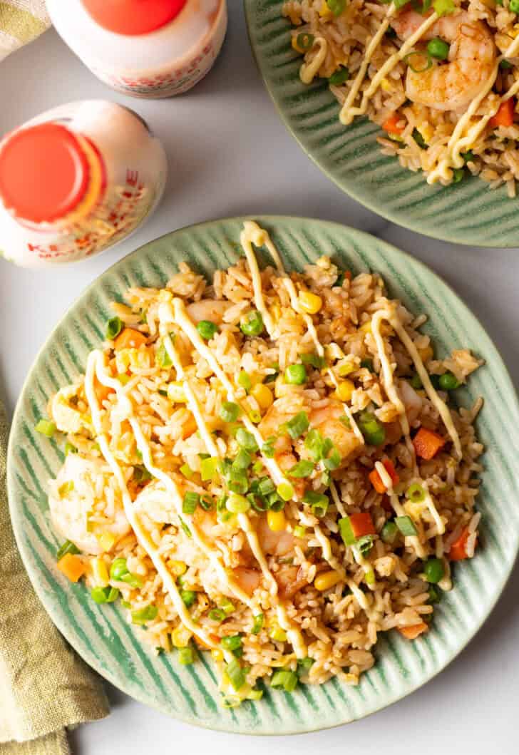 Top down view of a green plate piled with shrimp fried rice, topped with a zig zag drizzle of yum yum sauce.