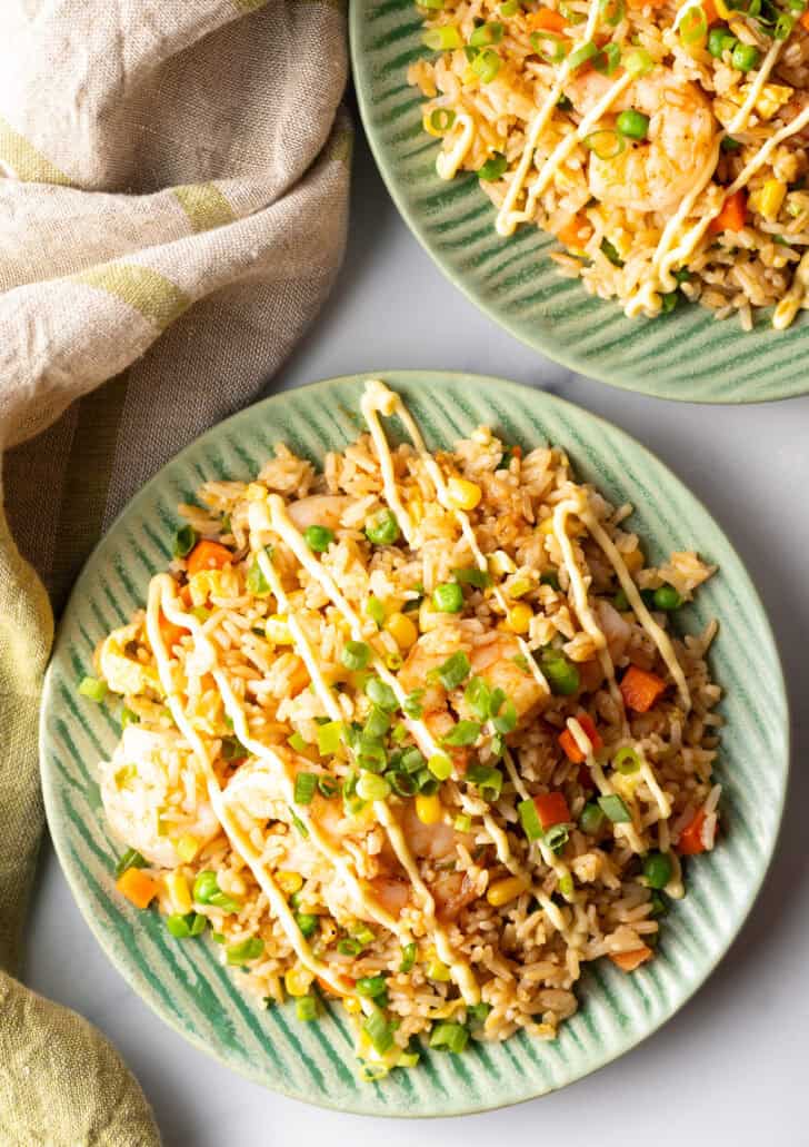 Top down view of a green plate piled with shrimp fried rice, topped with a zig zag drizzle of yum yum sauce.