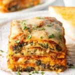 Square of cheesy spinach lasagna on a white plate.