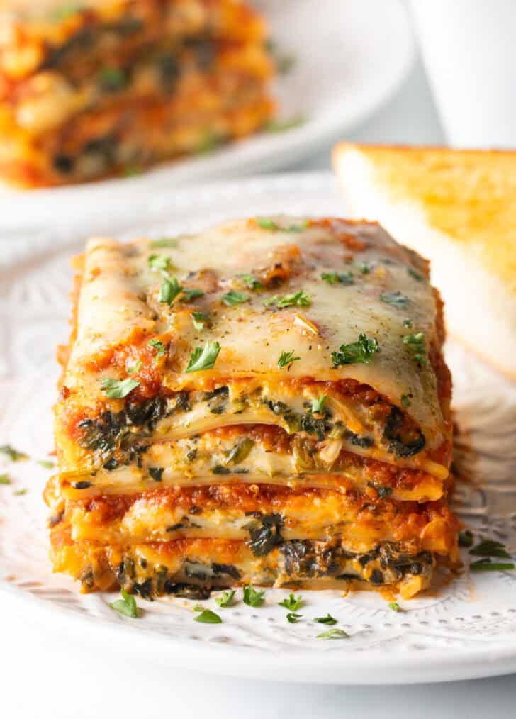 Square of cheesy spinach lasagna recipe on a white plate.