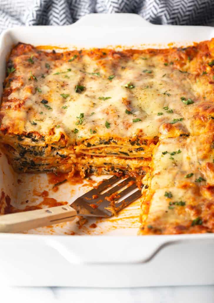 Baked vegetarian lasagna in a large white rectangle baking dish. Several servings have been removed from the dish with a metal spatula.