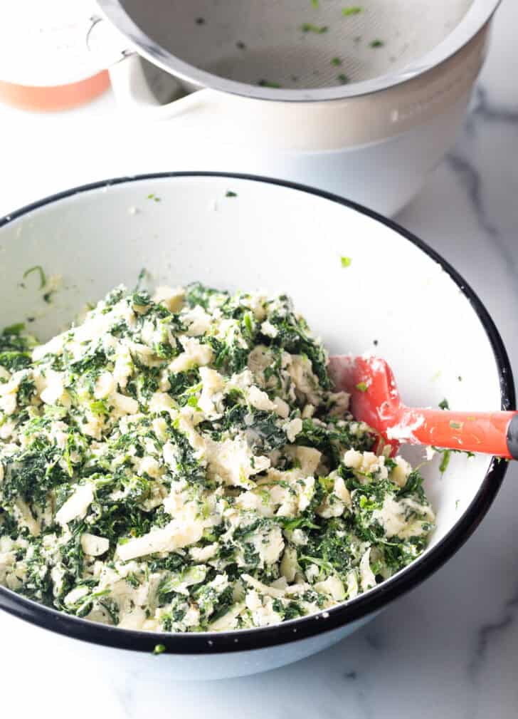 White mixing bowl with combination of spinach, cream cheese and Italian cheeses.