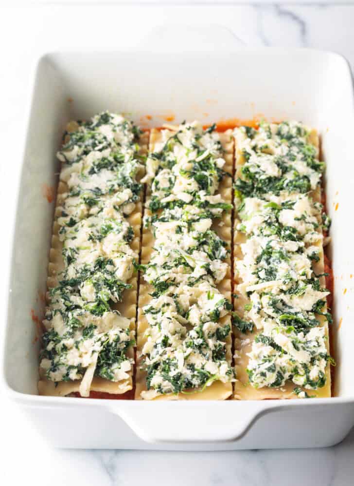 Layers in a large white rectangle baking dish, the layer shows creamy spinach and cheese spread across noodles.